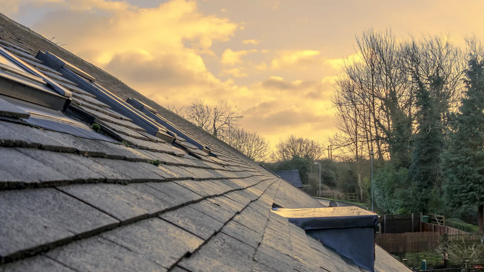 Skylights and a shingled roof slope beneath warm sunset clouds