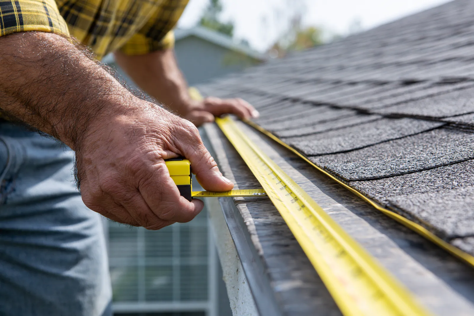 A roof edge is measured by a roofer with a yellow tape measure