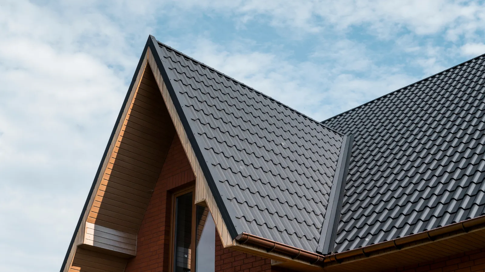 Brick wall below a steep gable clad in dark metal roof tiles